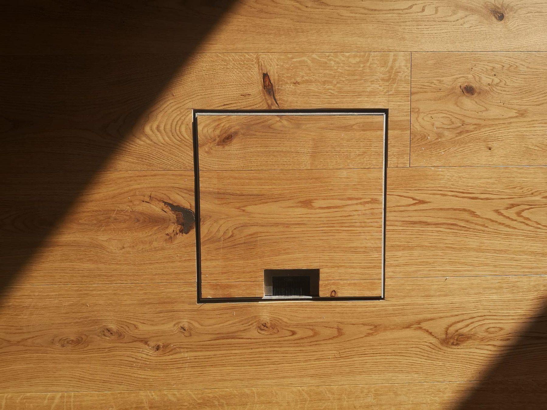 Trappe intégrée au parquet, photographiée dans la lumière du soleil